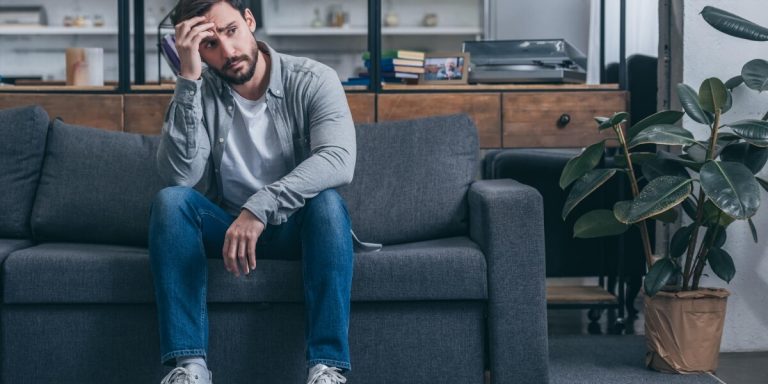 Man sitting on a sofa looking worried. He looks like he's been ghosted after an interview