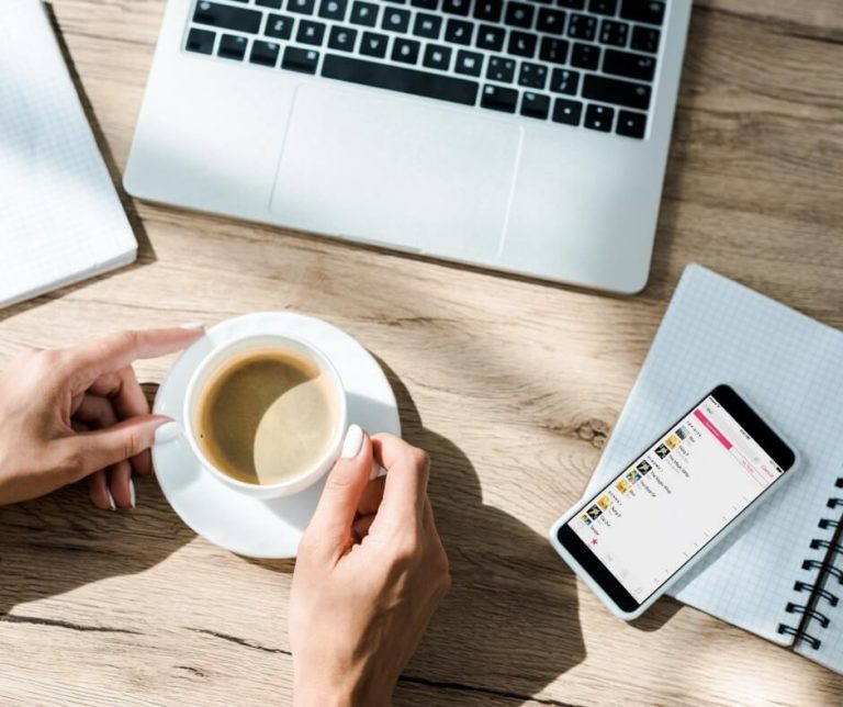 A lady having a cup of coffee in the sunshine whilst using social media to find top candidates on her laptop and phone simultaneously