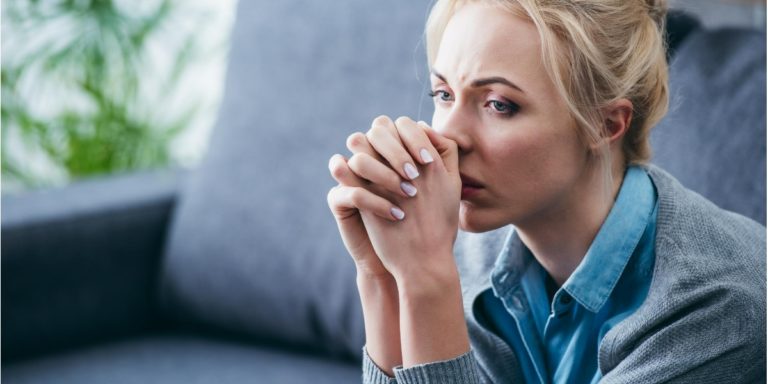 a woman sat on a sofa looks worried and thinking about something