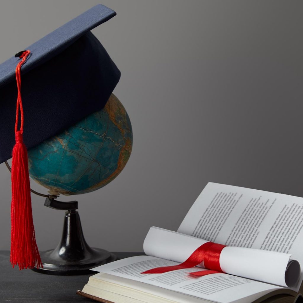 A globe wearing a mortarboard and an open book containing a scroll wrapped with a red ribbon.