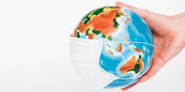 A hand holding a globe wearing a surgical mask