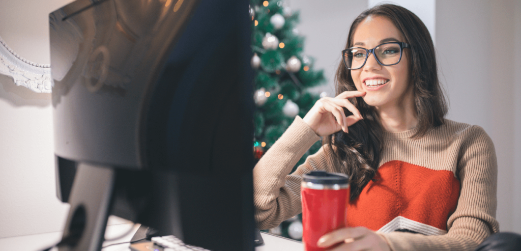 Lady smiling at her computer while drinking something festive