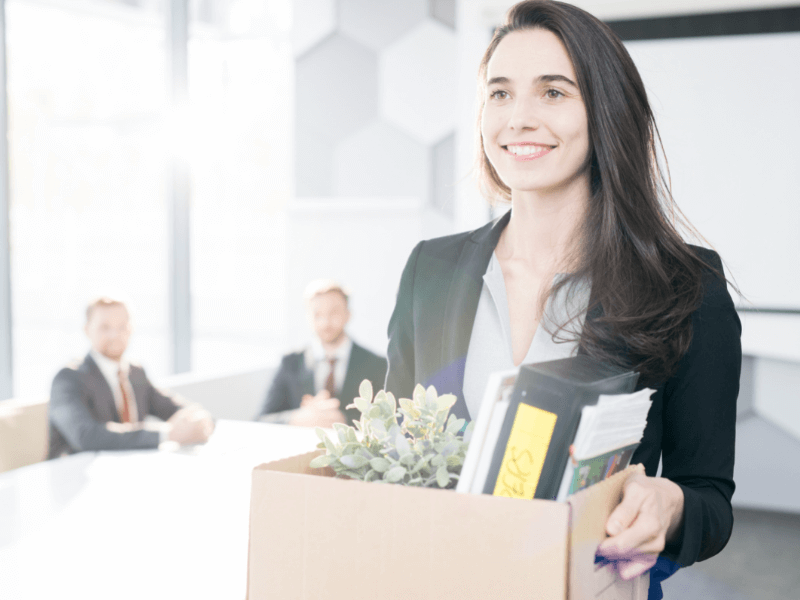 Young lady leaving her job with belongings packed in a box and a big smile on her face