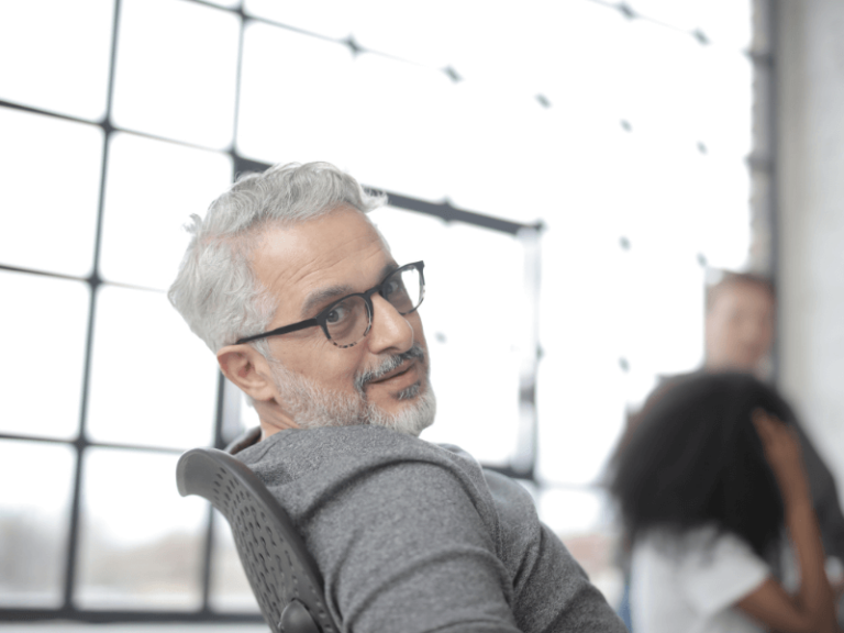 Employer looks right at the camera from his chair in front of a huge window