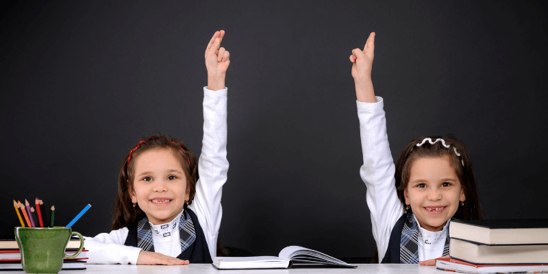 Eager young female students with their hands up in class