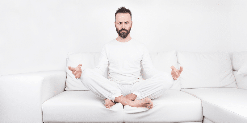 Man meditating intensely in a white suit on a white sofa in a white room