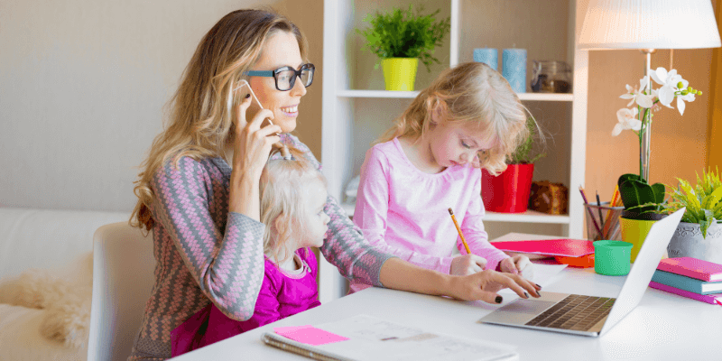 Lady working from home while children entertain themselves at her desk