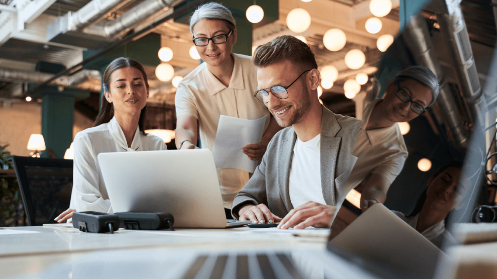 Newly hired tech team chat around a computers. This company understands the need to keep hiring tech talent during a recession.