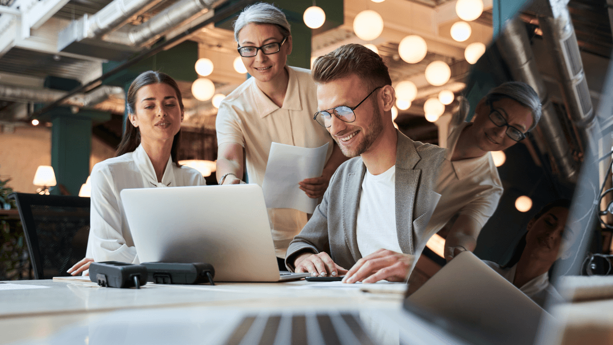 Newly hired tech team chat around a computers. This company understands the need to keep hiring during a recession.