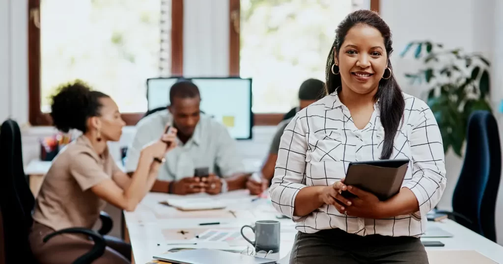 A woman holds an iPad while smiles in her office after a successful career switch to tech