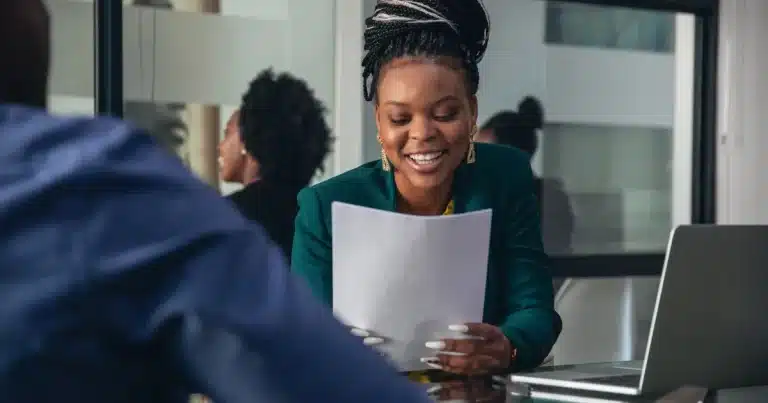 A black woman recruiter smiles after reading a perfectly-polished CV from a candidate