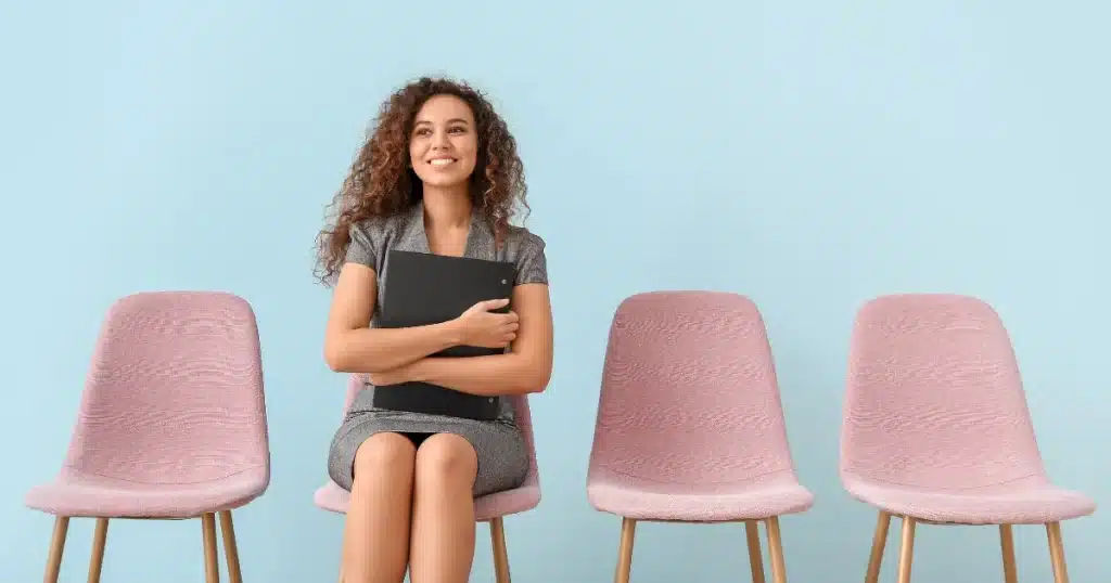 A woman smiles as she wait for her job interview. She is not worried, having chosen the right interview outfit.