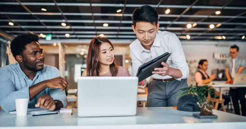 A black male, an asian female and an asian male work together in a vibrant office environment