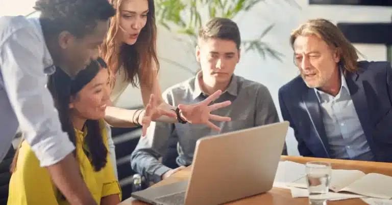 a woman explains her marketing strategy to the younger members of a team, while a marketing director looks at her laptop