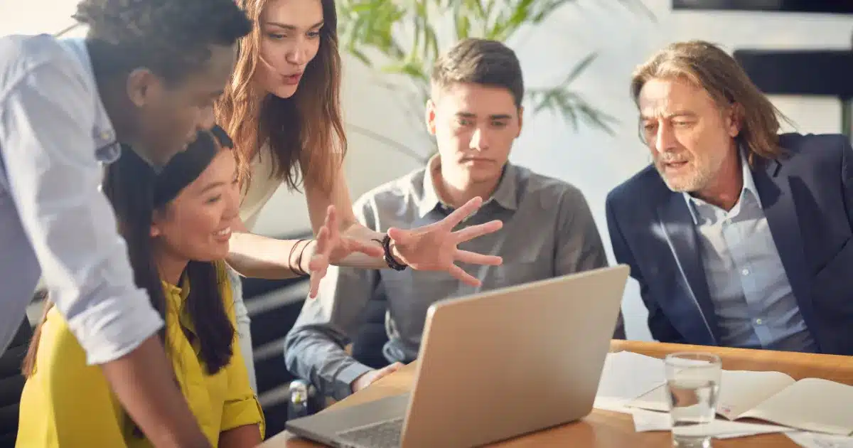 a woman explains her marketing strategy to the younger members of a team, while a marketing director looks at her laptop