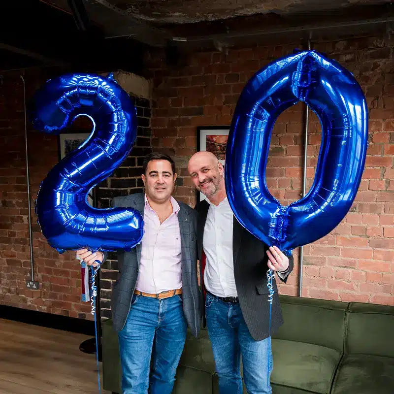 Nick and Dave hold a blue "20" balloon to celebrate Adria's 20 years in business