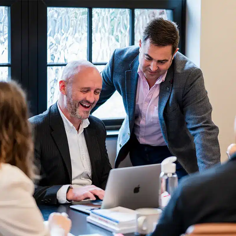 David an Nick smile, looking at Dave's laptop to read a very positive review a client has left of the company.